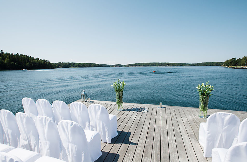 soligt bryggdäck med vita stolar uppradade på Villa Soludden