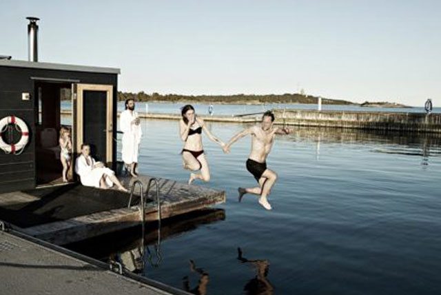 Personer hoppar i vattnet från bastuflotte på Sandhamn